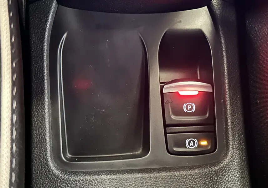 Gros plan sur la console centrale de la Renault Clio V hybride, avec bouton de frein à main électronique et indicateurs lumineux.