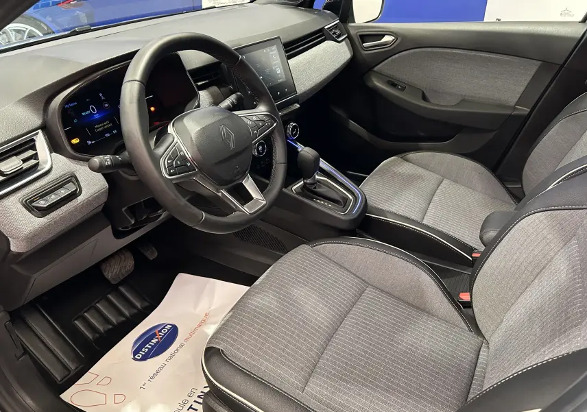 Vue intérieure côté conducteur de la Renault Clio V hybride, avec sièges gris tissu et tableau de bord moderne.