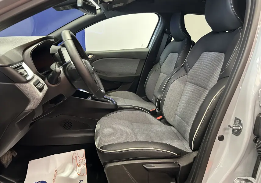 Vue intérieure côté conducteur de la Renault Clio V E-Tech gris Rafale, sièges tissu gris avec surpiqûres blanches.