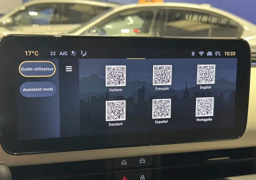 Écran tactile central de la FIAT 600 Hybrid 2024 affichant un guide utilisateur multilingue avec QR codes, vue intérieure.