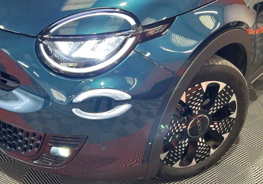 Gros plan sur l'avant droit bleu métallisé du FIAT 600 Hybrid 100 La Prima avec phare LED et jante au design moderne.