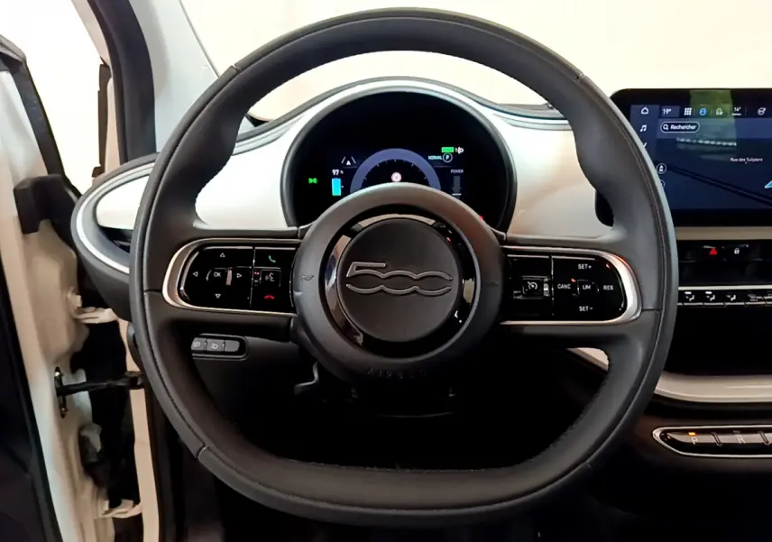 Vue rapprochée du volant noir de la Fiat 500 électrique blanche avec tableau de bord digital et écran tactile central.