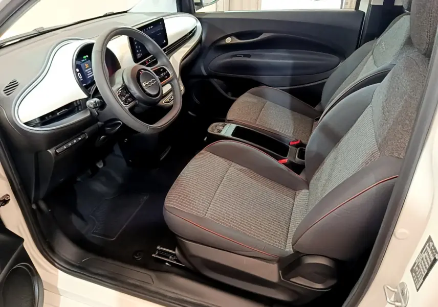 Intérieur côté conducteur de la Fiat 500 électrique blanche 2022, avec tableau de bord blanc et sièges gris à surpiqûres rouges