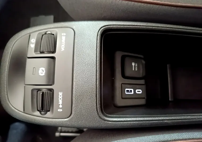 Gros plan sur la console centrale noire de la Fiat 500 électrique blanche, montrant commandes volume, mode et ports USB.