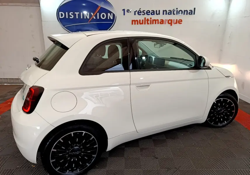 Profil côté droit d'une FIAT 500 électrique blanche 42kWh Icône avec jantes noires et vitres teintées en intérieur showroom