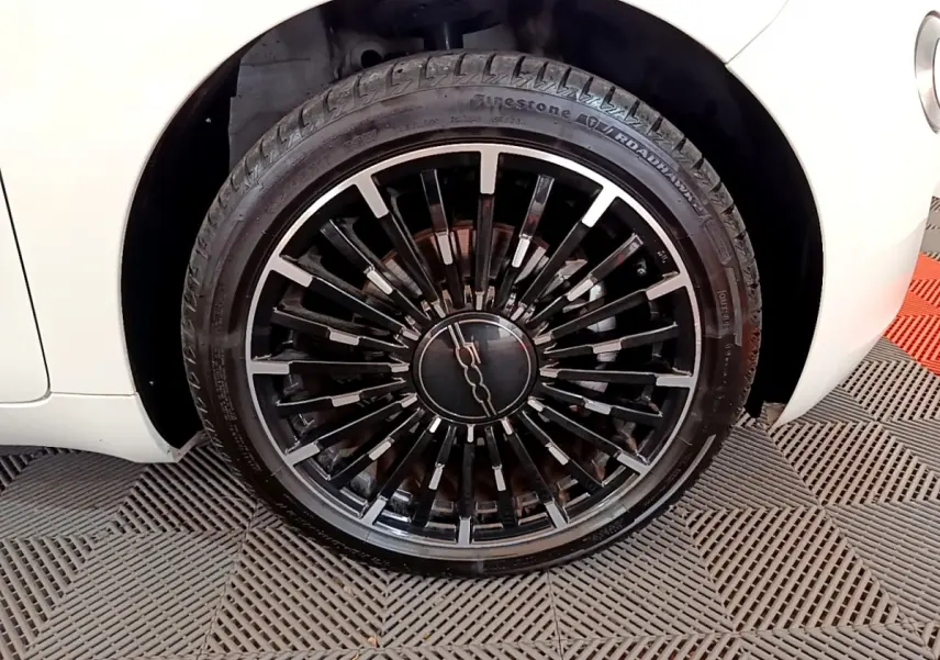 Gros plan sur la roue avant droite noire à jante stylisée du Fiat 500 blanc électrique 42kWh Icône 2022.
