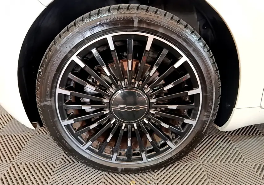 Gros plan sur la roue avant droite noire à jante multibranches du FIAT 500 blanc électrique 42kWh Icône 2022.