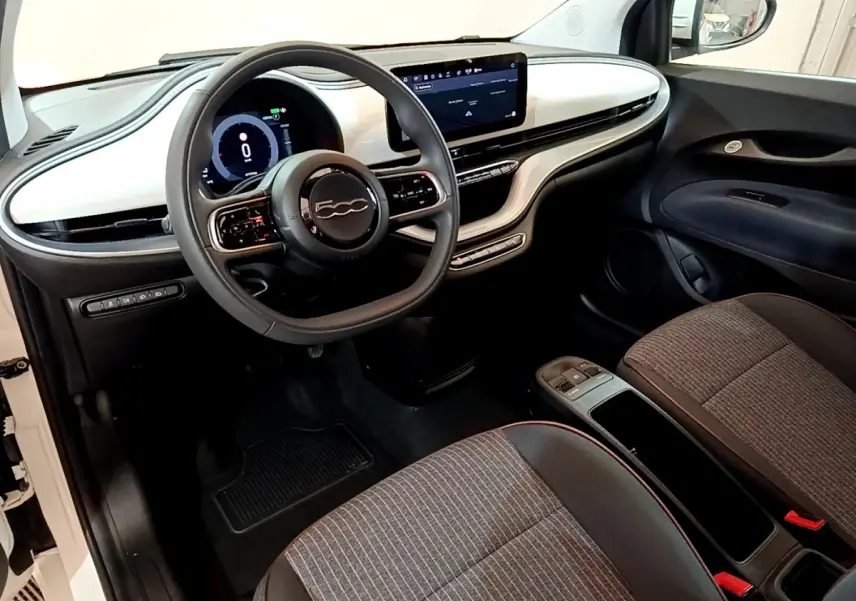 Intérieur avant de la Fiat 500 électrique blanche, vue côté conducteur, tableau de bord moderne avec écran tactile central.