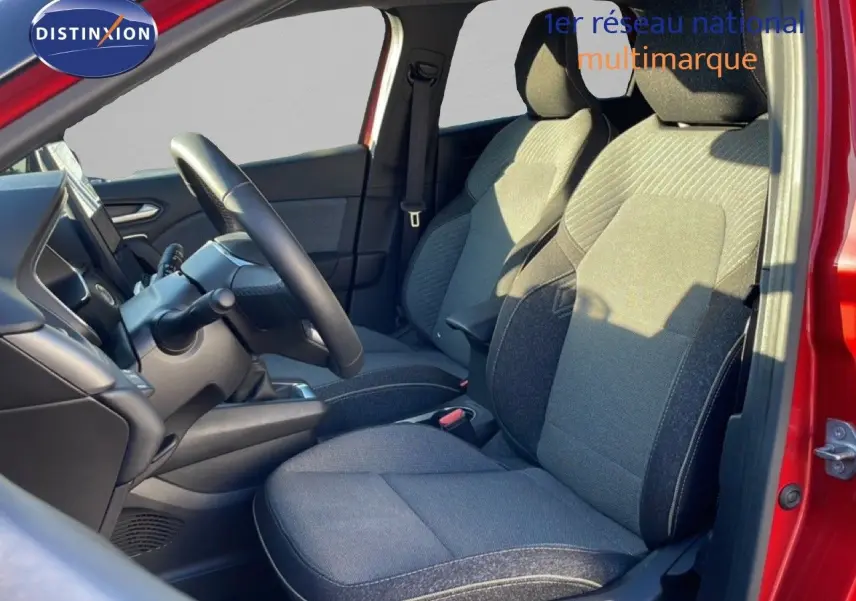 Vue intérieure côté conducteur du Renault Captur rouge désir métal, montrant les sièges en tissu gris et le volant.