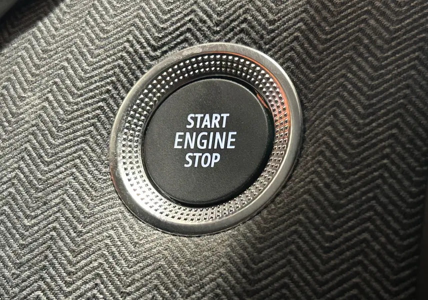 Gros plan sur le bouton Start Engine Stop entouré d'un cerclage métallique, sur un tableau de bord à motif chevrons gris.