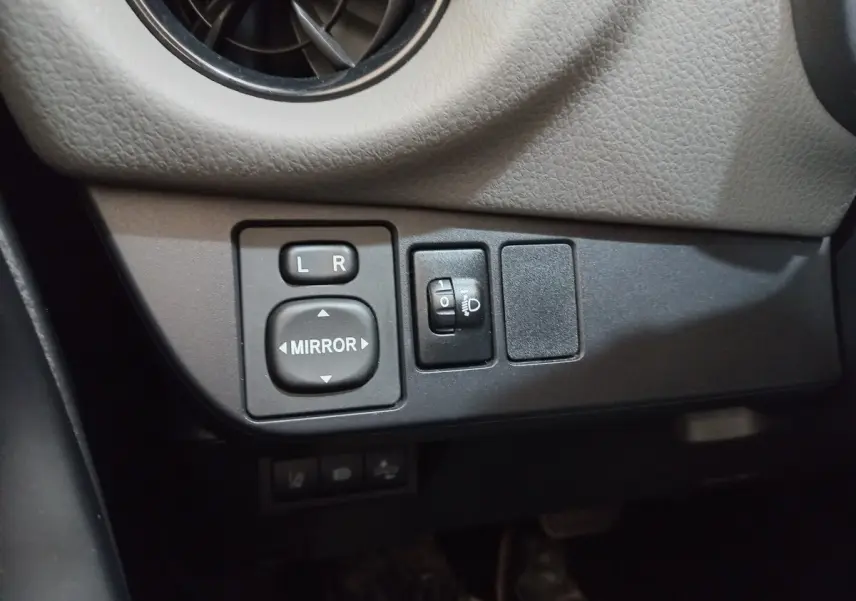 Vue rapprochée des commandes de réglage des rétroviseurs et des phares sur la Toyota Yaris blanche 2019.