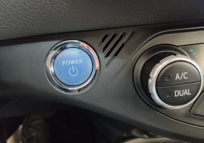 Gros plan sur le bouton bleu Power et la commande de climatisation dual de l'intérieur d'une Toyota Yaris blanche hybride.