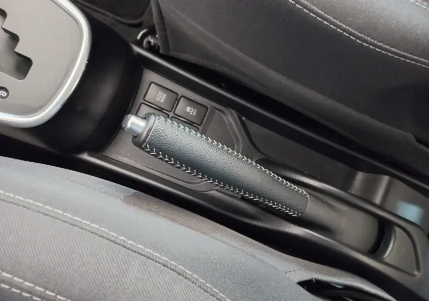 Vue rapprochée de la poignée de frein à main en cuir noir avec surpiqûres blanches dans l'habitacle de la Toyota Yaris hybride blanche.
