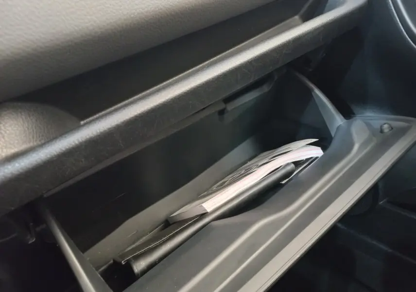 Gros plan sur la boîte à gants ouverte de la Toyota Yaris 1.5 VVT-I HYBRID France Business, intérieur noir.