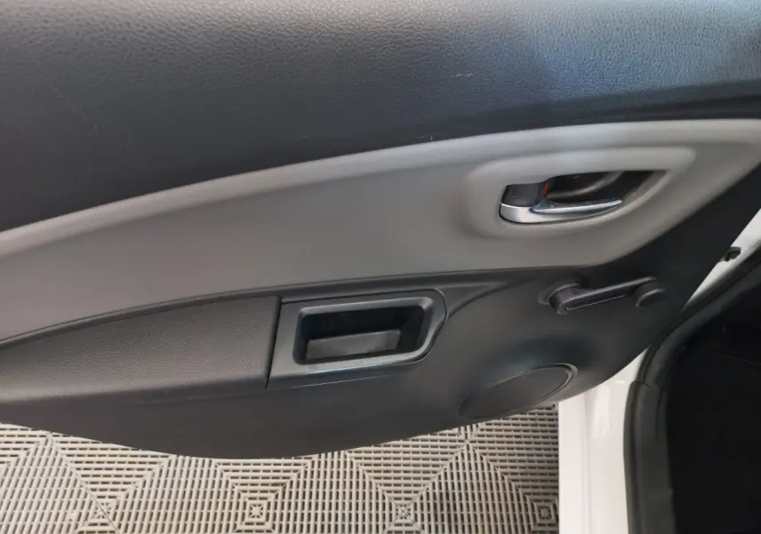 Gros plan sur la porte intérieure côté droit d'une Toyota Yaris blanche, avec poignée chrome et manivelle de vitre.