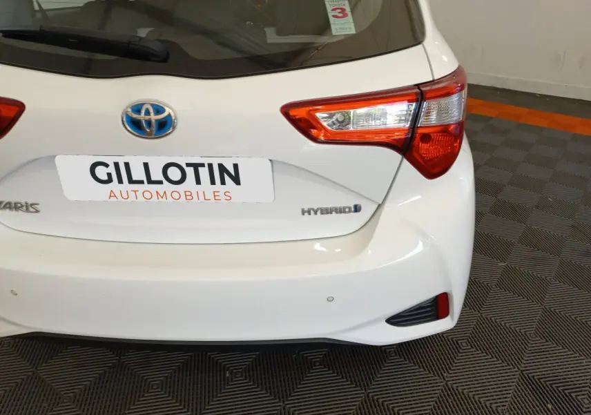 Vue arrière droite d'une Toyota Yaris blanche hybride avec feux arrière distinctifs et logo bleu Toyota.