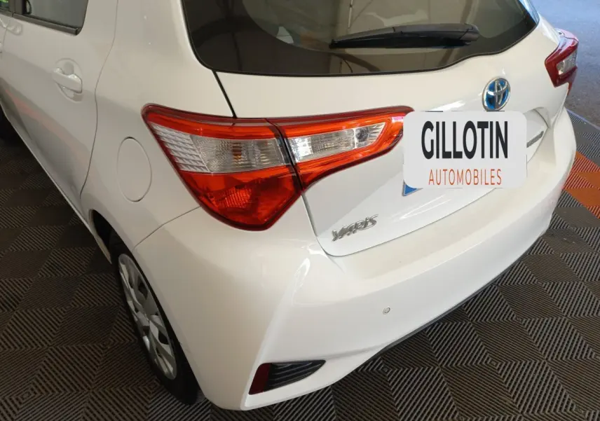 Vue 3/4 arrière gauche d'une Toyota Yaris blanche avec feux arrière distinctifs et badge modèle visible