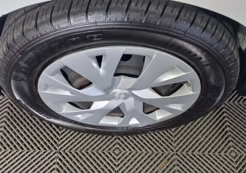 Gros plan sur la roue avant droite d'une Toyota Yaris blanche, avec jante argentée et pneu Dunlop visible.