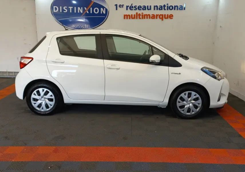 Profil côté gauche d'une Toyota Yaris blanche hybride 2019, avec jantes standard et logo Hybrid visible sur l'aile avant.