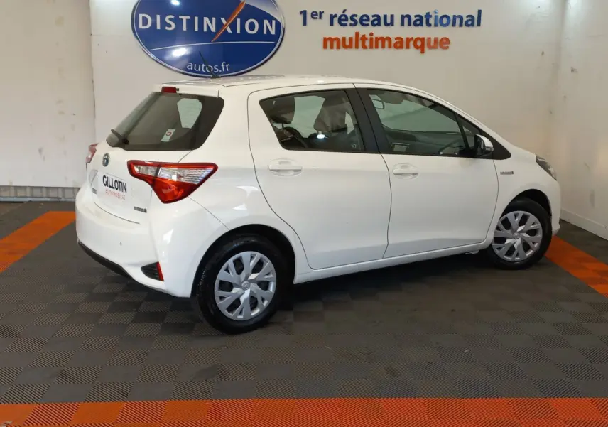 Toyota Yaris blanche vue de profil côté droit dans un showroom avec logo Distinxion en arrière-plan.