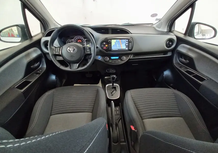 Vue intérieure avant de la Toyota Yaris 1.5 Hybrid 2019, tableau de bord noir avec écran tactile et sièges tissu gris.