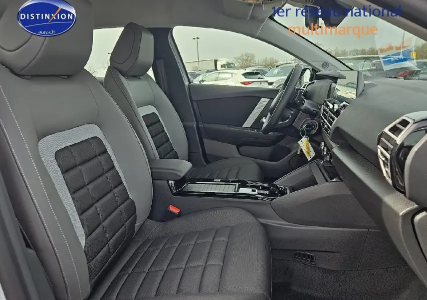 Vue intérieure côté conducteur de la Citroën C4 hybride 2025 avec sièges tissu noir et gris et console centrale noire brillante.