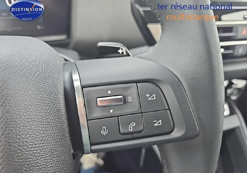 Gros plan sur les commandes audio au volant en cuir noir de la Citroën C4 hybride 2025, intérieur moderne.