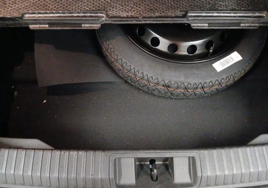 Vue rapprochée du coffre du Renault Symbioz 2025 bleu iron, montrant la roue de secours et le tapis noir.