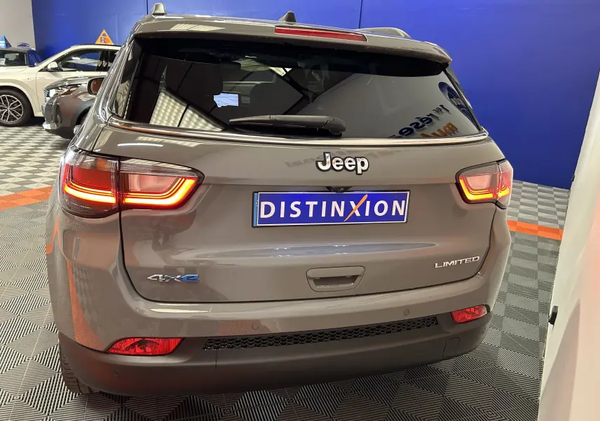 Vue arrière d'un Jeep Compass gris 2021 Limited 4xe avec feux allumés et logo 4xe bleu visible.