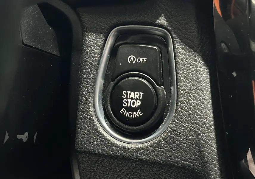 Gros plan sur le bouton Start Stop Engine noir entouré de cuir noir dans une BMW Série 3 blanche de 2018.