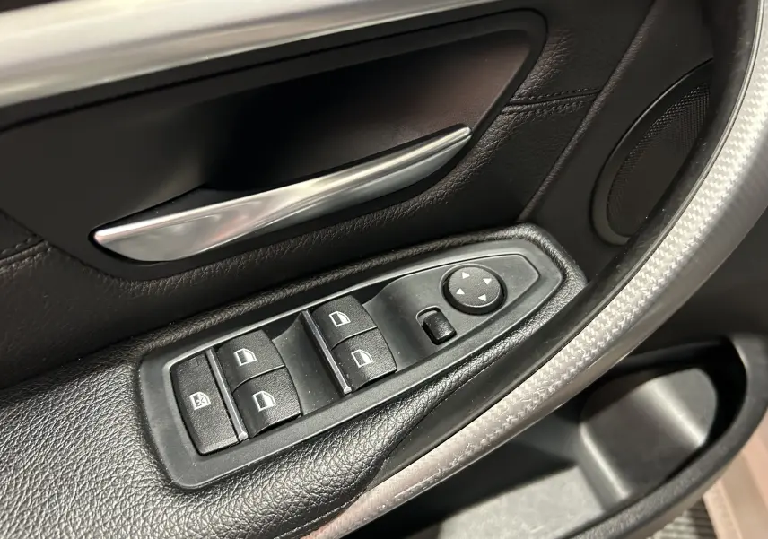 Gros plan sur les commandes de lève-vitres et rétroviseurs côté conducteur d'une BMW Série 3 blanche 320i 2018.