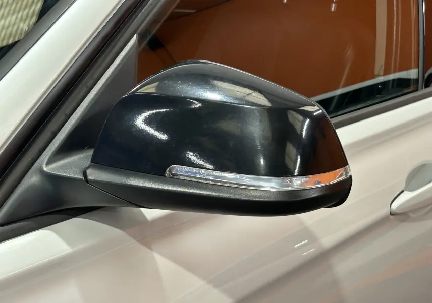 Rétroviseur extérieur noir côté gauche d'une BMW Série 3 320i blanche, vue rapprochée sur la portière avant.