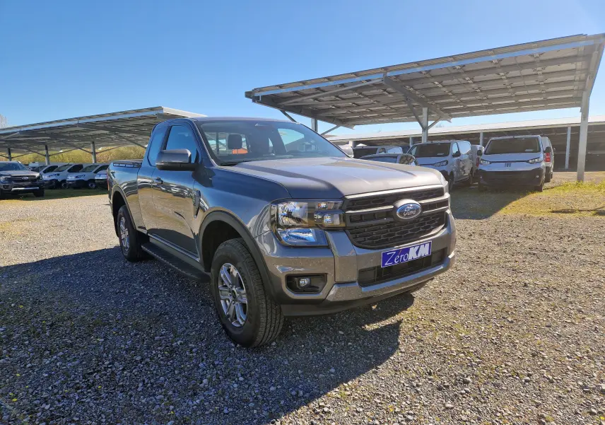 Vue 3/4 avant droit d’un Ford Ranger Super Cabine gris carbone diesel, stationné sur un terrain gravillonné en plein jour.