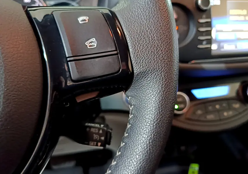 Gros plan sur le volant cuir noir de la Toyota Yaris hybride 2020 avec commandes intégrées et tableau de bord flou en arrière-plan