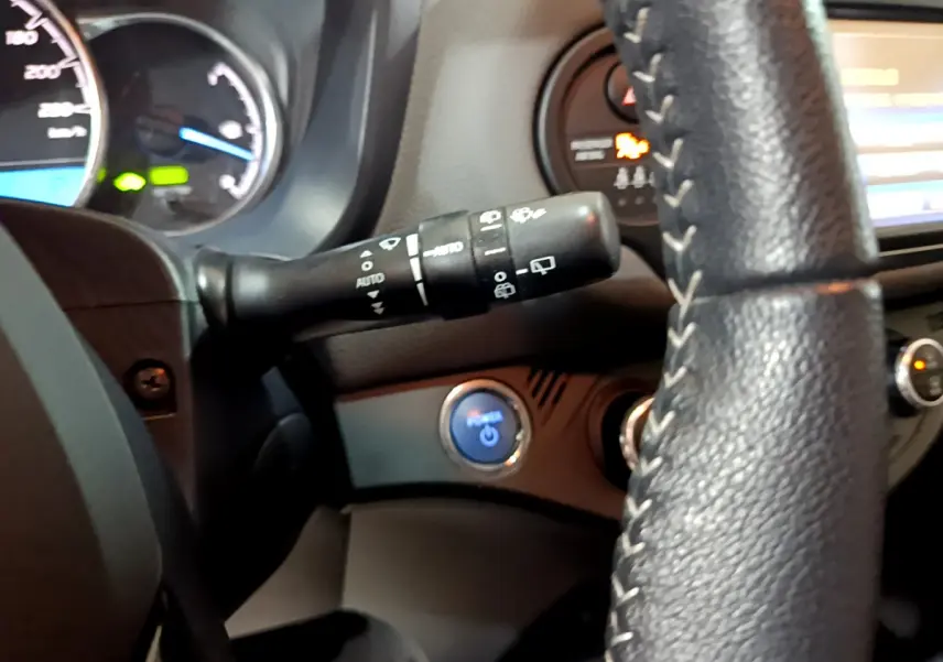Détail du commodo d'essuie-glace et bouton démarrage bleu sur le tableau de bord d'une Toyota Yaris hybride blanche, vue intérieure côté conducteur.
