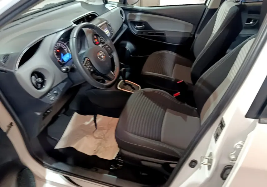 Intérieur avant gauche d'une Toyota Yaris blanche 2020, sièges tissu noirs et tableau de bord avec écran tactile.