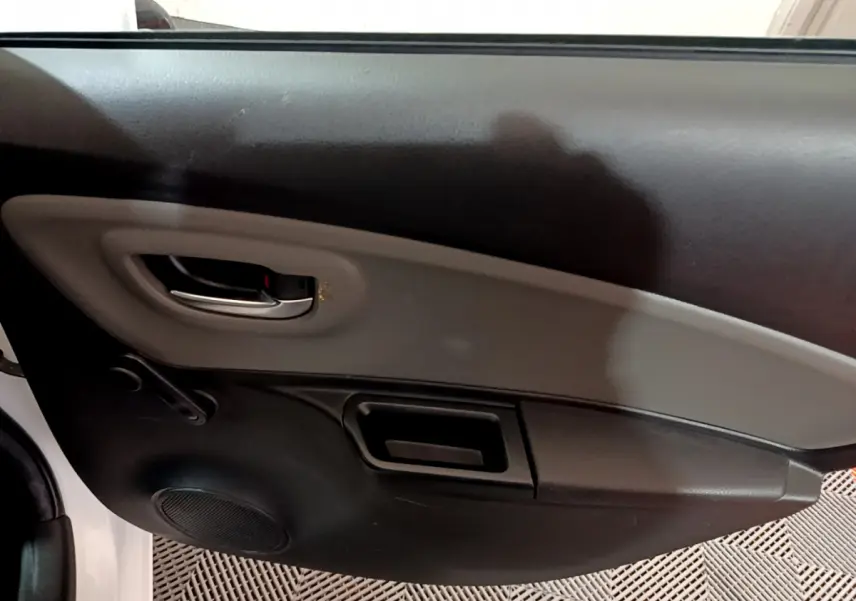 Vue rapprochée de la porte côté gauche de la Toyota Yaris blanche, montrant la poignée intérieure et le haut-parleur intégré.