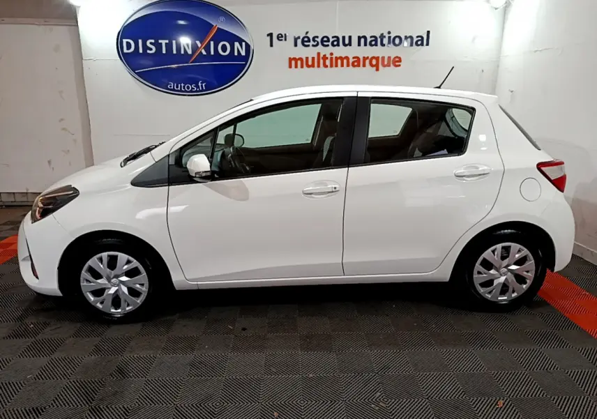 Profil côté gauche d'une Toyota Yaris blanche 2020 1.5 Hybride France Business en intérieur showroom.
