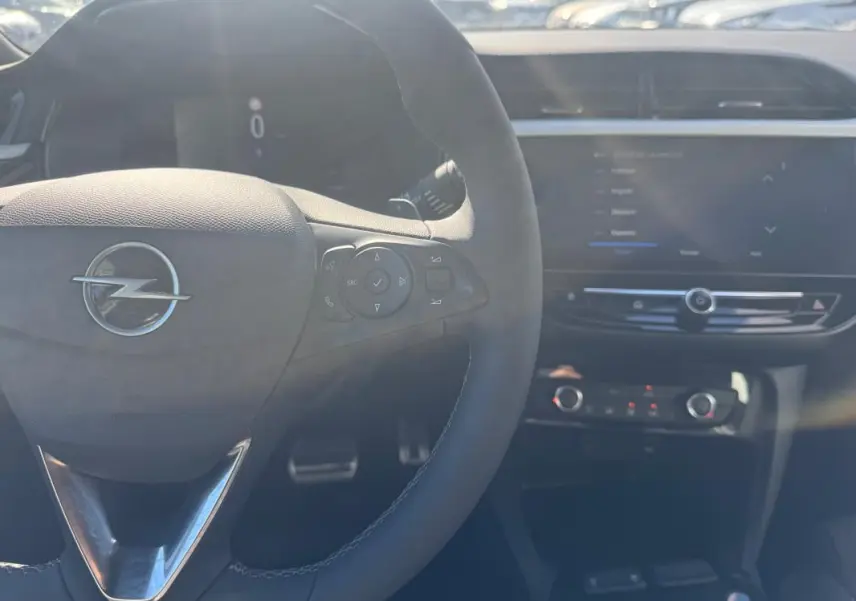 Vue intérieure centrée sur le volant Opel avec commandes intégrées et tableau de bord numérique flou en arrière-plan.