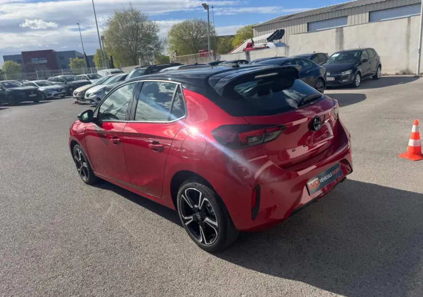 Vue 3/4 arrière droite d'une Opel Corsa rouge avec toit noir et jantes alliage 17 pouces, stationnée en extérieur.