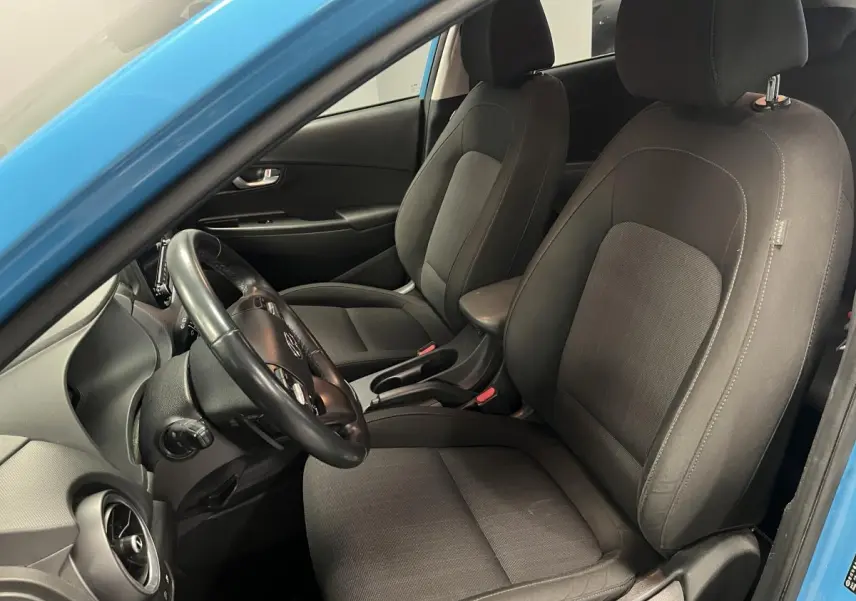 Vue intérieure côté conducteur du Hyundai Kona bleu 2022 montrant les sièges avant en tissu gris et le volant cuir.