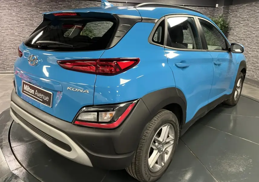 Vue 3/4 arrière droit d'un Hyundai Kona bleu avec protections noires et antenne aileron de requin.