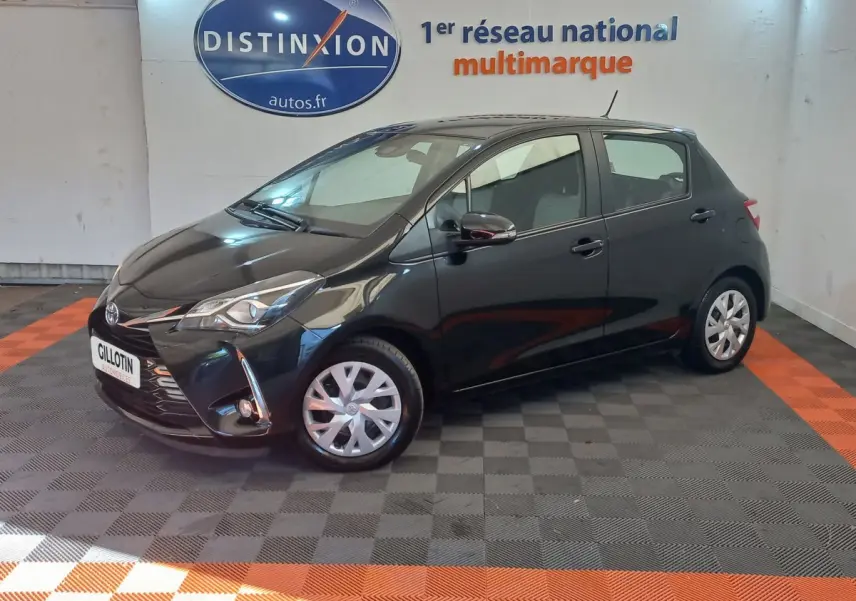 Toyota Yaris noire vue de profil côté gauche en intérieur, avec jantes argentées et phares allumés.