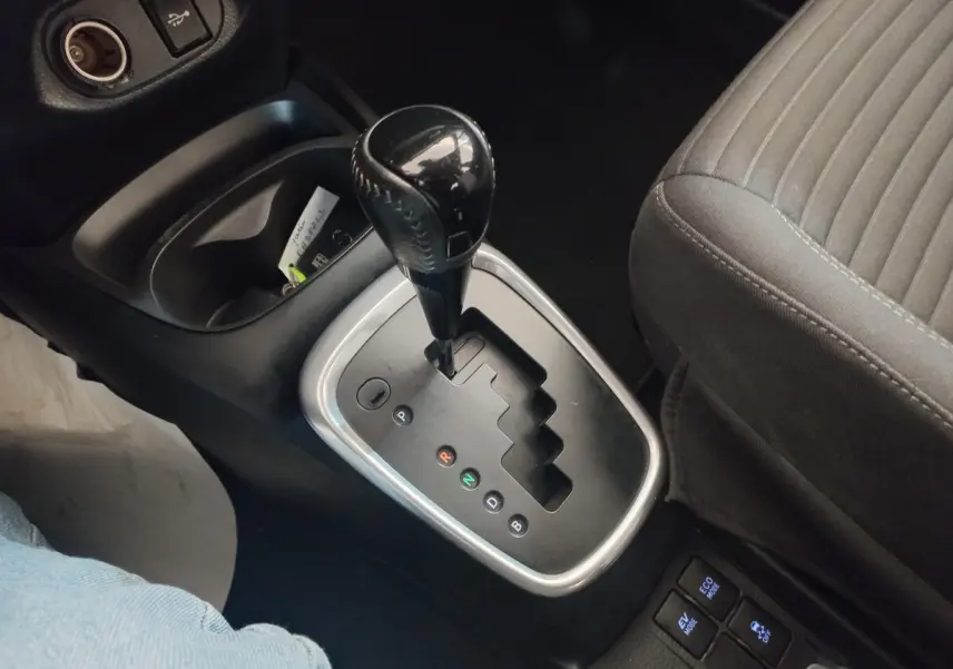 Le levier de vitesse automatique noir vu de dessus dans l'habitacle d'une Toyota Yaris noire, siège tissu gris visible.