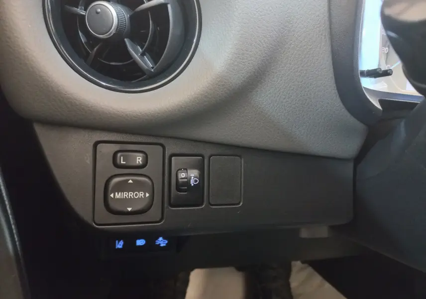 Gros plan sur les commandes de réglage des rétroviseurs et phares côté gauche du tableau de bord noir de la Toyota Yaris hybride 2018.