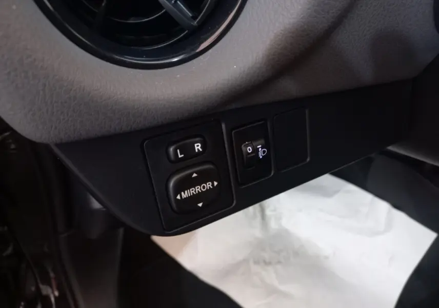 Gros plan sur les commandes de réglage des rétroviseurs côté gauche dans l'habitacle d'une Toyota Yaris noire 2018.