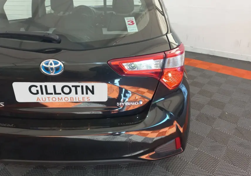Vue arrière droite d'une Toyota Yaris noire hybride avec logo Toyota et badge Hybrid visible sur le coffre.