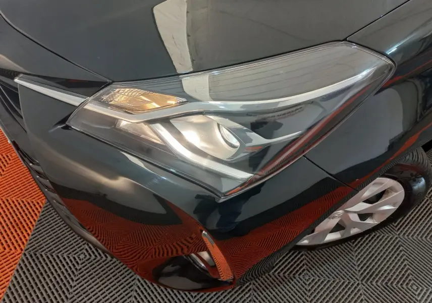 Gros plan sur le phare avant droit d'une Toyota Yaris noire, avec partie de la roue et pare-chocs visibles.