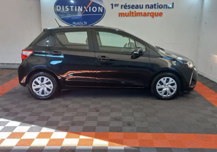 Profil côté gauche d'une Toyota Yaris noire 2018 en hybride, stationnée dans un showroom avec sol à damiers.