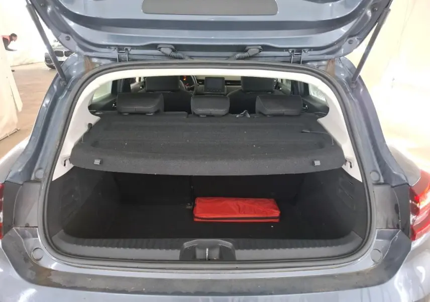 Coffre ouvert d'une Renault Clio 5P Business gris titanium, vue arrière montrant l'intérieur du coffre avec un objet rouge.